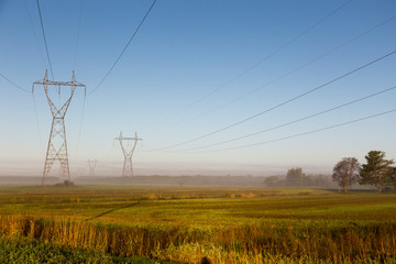View of power line towers in farmland fields during a beautiful misty late summer golden hour...
