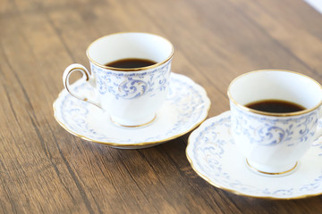Fototapeta na wymiar 木製テーブルの上に乗った白い陶器のカップ&ソーサーにブラックコーヒー
