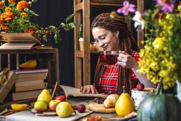 Woman reading romantic book in autumn atmosphere. Rustic table with yellow flowers and a stack of books. Fall mood
