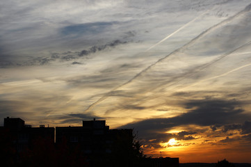Urban silhouette with colorful sky covered in contrails and clouds during sunrise.