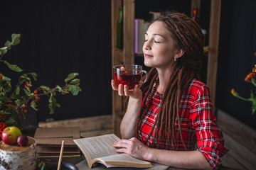 Woman reading a romantic book in a cozy warm atmosphere enjoying the autumn mood. Rustic table with stack of books