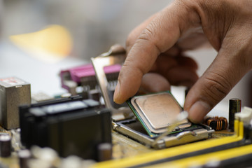 Assembling high performance personal computer, inserting CPU, processor into the motherboard socket, opened PC case in background.