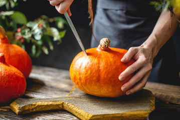 Woman chef cleans an orange pumpkin to prepare for baking. Autumn food in a cozy dark wooden...