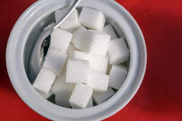 sugar cubes and spoon in a white bowl on a red background, high angle view from above