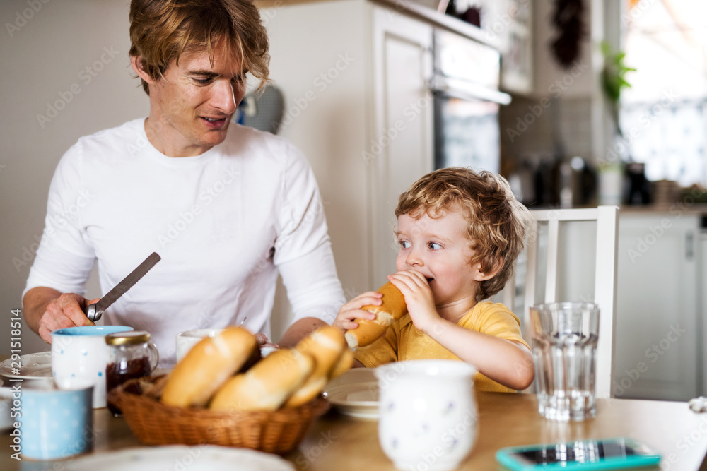 Wall mural young father with a toddler son eating breakfast indoors at home.