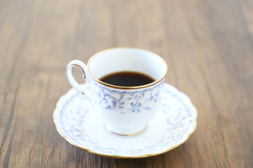 木製テーブルの上に乗った白い陶器のカップ&ソーサーにブラックコーヒー