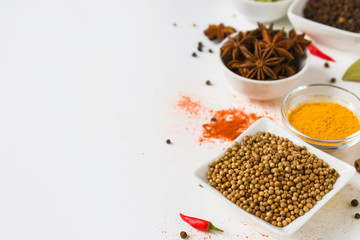 coriander in white bowl and colorful spices on a white background, with copy spice