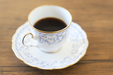 木製テーブルの上に乗った白い陶器のカップ&ソーサーにブラックコーヒー