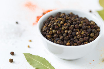 black papper corn in white bowl and colorful spices on a white background