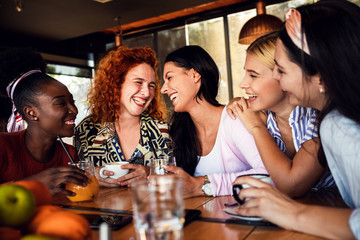 Group of young female friends having fun in cafe, talking and laughing while sitting at table.	