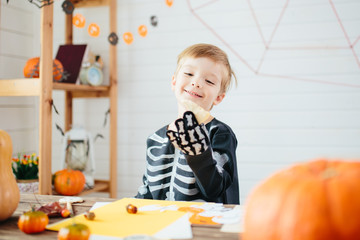 Fototapeta premium Happy young blond hair little boy in a skeleton costume is ready to celebrate Halloween. Boy in a halloween dress-up room.