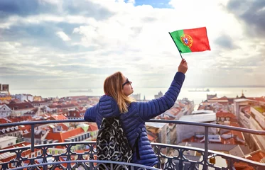 Fotobehang Young woman tourist enjoying beautiful cityscape top view on the old town holding the flag of Portugal in hands during the sunny day in Lisbon city © bondvit