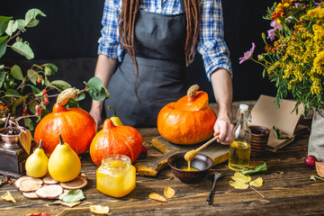 Woman chef reading a recipe in a book for cooking orange pumpkin. Concept autumn food in a cozy dark wooden kitchen