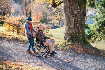 Senior father with wheelchair and his son on walk in nature.