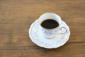 木製テーブルの上に乗った白い陶器のカップ&ソーサーにブラックコーヒー