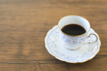 木製テーブルの上に乗った白い陶器のカップ&ソーサーにブラックコーヒー