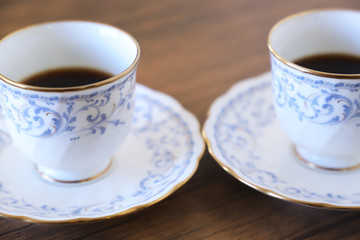 木製テーブルの上に乗った白い陶器のカップ&ソーサーにブラックコーヒー