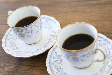 木製テーブルの上に乗った白い陶器のカップ&ソーサーにブラックコーヒー