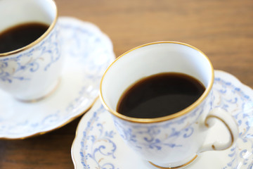 木製テーブルの上に乗った白い陶器のカップ&ソーサーにブラックコーヒー