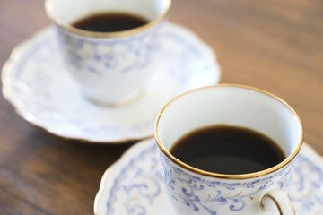 木製テーブルの上に乗った白い陶器のカップ&ソーサーにブラックコーヒー
