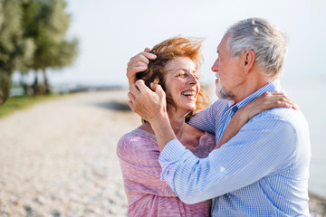 Senior couple on a holiday on a walk by the lake, hugging.