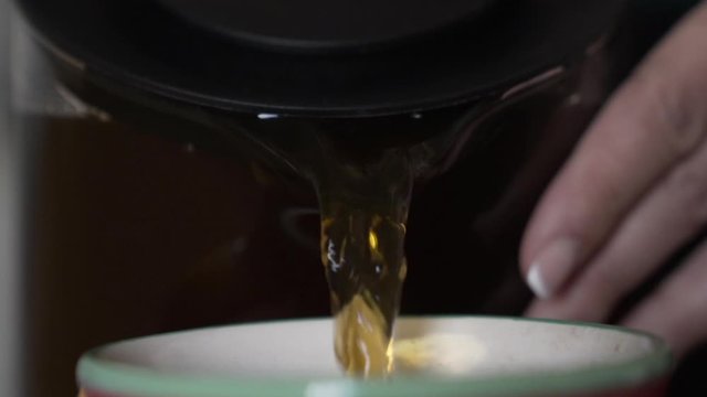 Upfront close shot as pouring out herbal tea from a pot toa mug.