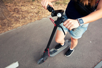Obraz premium The young woman is riding on the electric scooter through the evening city by the pathways