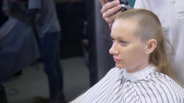 Woman shaving her head baldly. a hairdresser shaves a woman's long hair with a hair clipper.