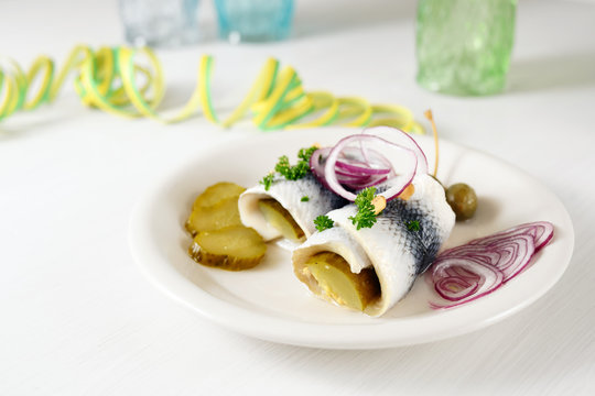hangover meal, rolled pickled herring, also called rollmops with red onions, gherkins and capers on a white table with paper streamers, copy space