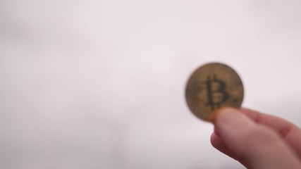 Hand Holding Up Bitcoin In Front Of Wind Turbine, England Cloudy Day - Powered by Adobe