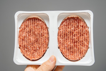 man hand holding fresh steak cutlets in white plastic recipients against gray background