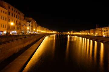 Fototapeta na wymiar Illuminated shores on the river Arno in Pisa at night, dark and lively location for summer nightlife, used by students, tourists and young people, long exposure shot, copy space
