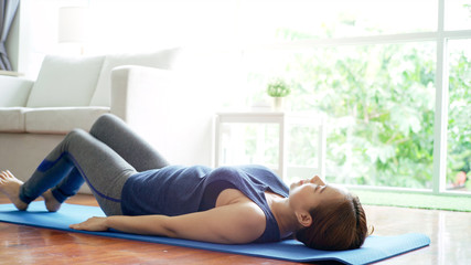 Asian mother teaching her daughter and practicing light yoga exercise stretching movements on a mat learning to control various parts of the body in the brightly lit sunny morning living room. Concept