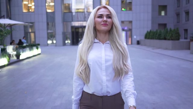 Blond smiling caucasian businesswoman walking on the city street and smiling. Young professional going for lunch.