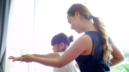 Asian mother teaching her daughter and practicing light yoga exercise stretching movements on a mat learning to control various parts of the body in the brightly lit sunny morning living room. Concept