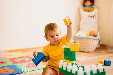 Fototapeta premium little girl playing with construction toy blocks building a tower in a sunny kindergarten room