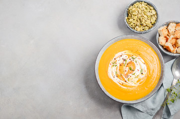 Pumpkin soup with cream, croutons, pumpkin seeds and thyme on a gray concrete or stone background Top view Flat lay Copy space
