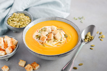 Pumpkin soup with cream, croutons, pumpkin seeds and thyme on a gray concrete or stone background