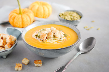 Pumpkin soup with cream, croutons, pumpkin seeds and thyme on a gray concrete or stone background