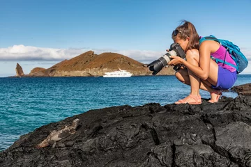 Foto op Canvas Galapagos tourist photographing marine iguana on Santiago Island in Galapagos Islands. Cruise ship and Pinnacle Rock and Bartolome Island in background. Famous Galapagos cruise ship tour destination. © Maridav