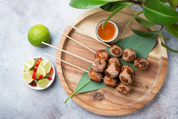 Top view of a round bamboo tray with fried vietnamese nem nuong skewers and fish sauce, horizontal shot on a beige stone background