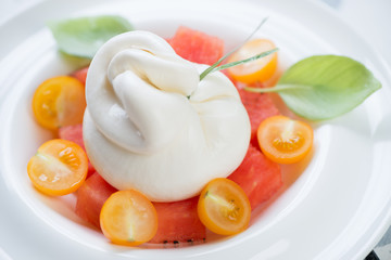 Close-up of burrata cheese with yellow cherry tomatoes and watermelon cubes, studio shot