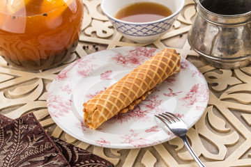 sweet wafer tube from thin dough and glass of black tea on oriental wooden table