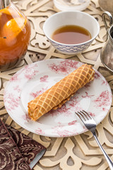 sweet wafer tube from thin dough and glass of black tea on oriental wooden table