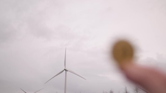 Someone Holding A Bitcoin In Front Of A Wind Turbine - Powered by Adobe