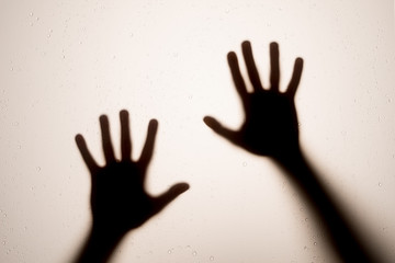 Scared person's Arms Silhouette behind frosted window, beating on window and trying to get out. Ghost like figure.