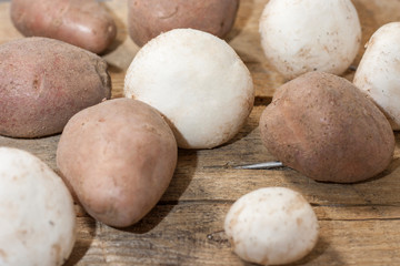 Bunch of champignon mushrooms and potatoes on wooden background close-up.