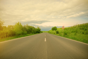 Fototapeta premium Road sign indicating left turn, blue sky with clouds and green trees 