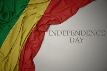 waving colorful national flag of republic of the congo on a gray background with text independence day.