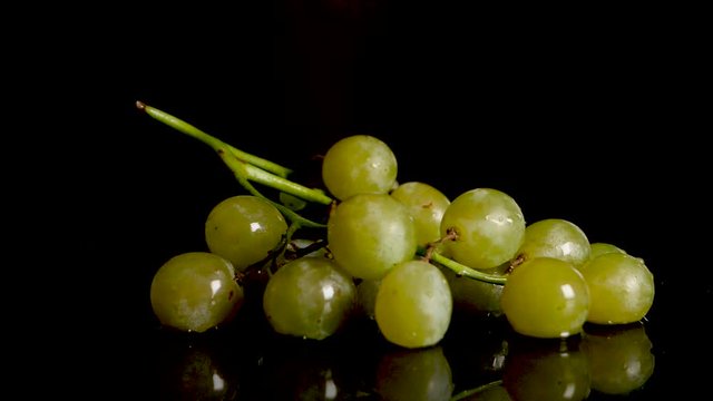 Green Grapes Falling On Water Surface Against Black Background. Slow Motion